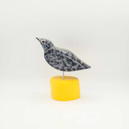 Oiseau gris sur socle jaune