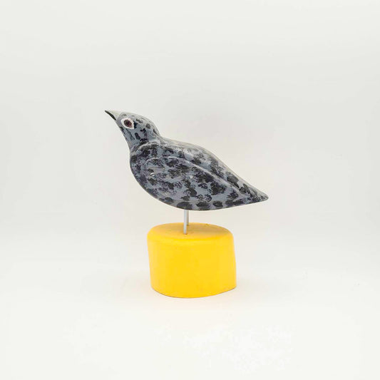 Oiseau gris sur socle jaune